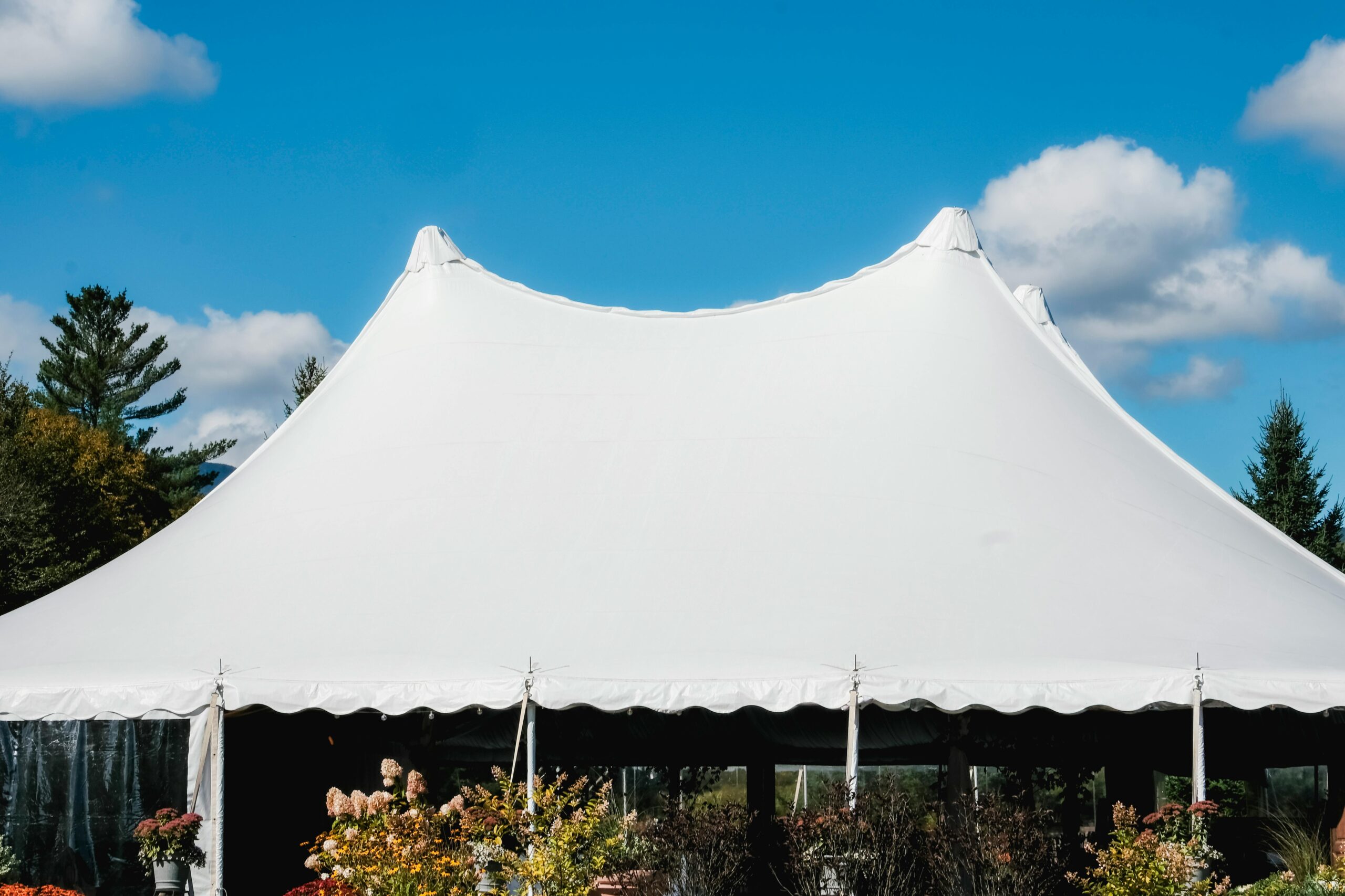 A sleek white tent set up outdoors under a vibrant blue sky with fluffy clouds.