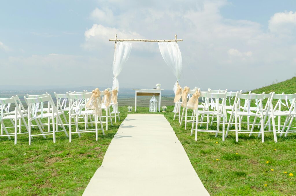 Elegant outdoor wedding setup with chairs and arch under a blue sky.